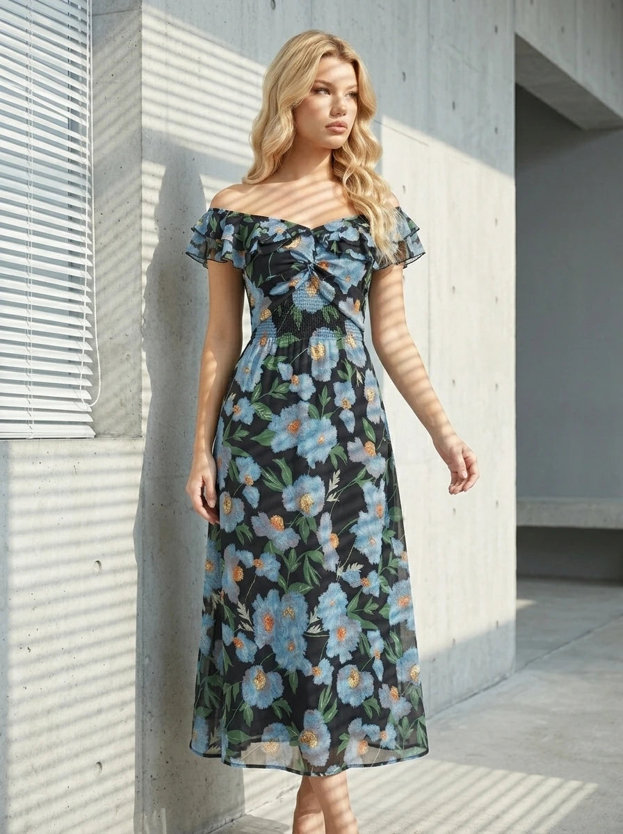 Woman standing outdoors wearing a black floral print off-the-shoulder midi dress with blue flowers, with shadows on the wall