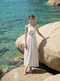 Woman wearing a white halter neck midi dress standing on rocks by the sea