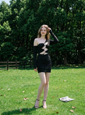 Woman in a black cut-out mini dress posing in a grassy outdoor setting.