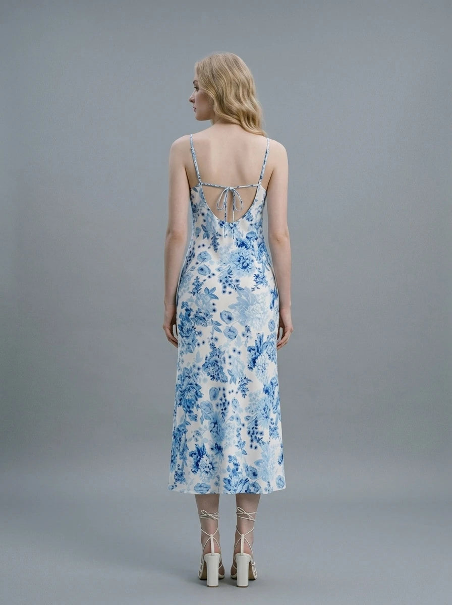 Woman wearing a white slip dress with a blue floral print, spaghetti straps, cowl neckline, and a high side slit.