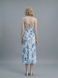 Back view of a woman in a white slip dress with a blue floral print, showing the open back with tie detail and spaghetti straps.