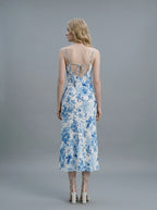 Back view of a woman in a white slip dress with a blue floral print, showing the open back with tie detail and spaghetti straps.