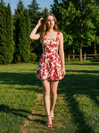 Woman wearing a red and white floral print sleeveless fit and flare dress with a square neckline, walking in a park.