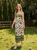 Woman wearing a white midi dress with a green smocked bodice and a colorful bird and floral print, walking in a grassy garden.