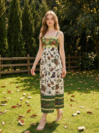 Woman wearing a white midi dress with a green smocked bodice and a colorful bird and floral print, walking in a grassy garden.