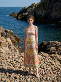 Woman wearing a printed midi sundress standing on a rocky beach with the ocean in the background.