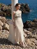Woman wearing a cream knit maxi dress with black striped bodice, standing by the sea