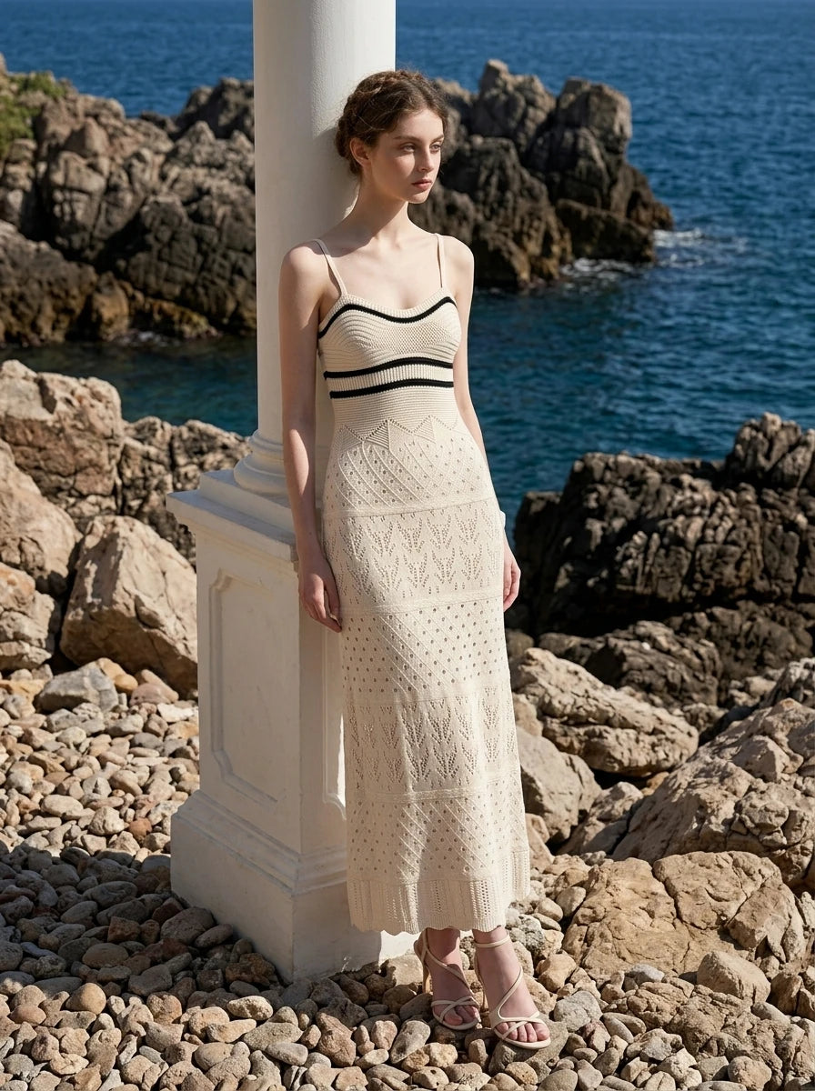 Woman wearing a cream knit maxi dress with black striped bodice, standing by the sea
