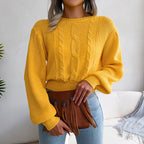 Woman holding a brown fringed clutch while wearing a yellow cable knit cropped sweater and jeans.