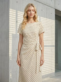 Woman standing outdoors wearing a cream polka dot midi wrap dress