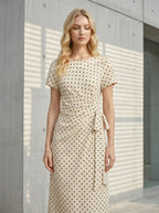 Woman standing outdoors wearing a cream polka dot midi wrap dress