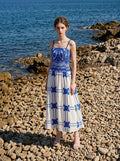 Woman wearing a pink midi dress with a tropical print and spaghetti straps on a rocky beach