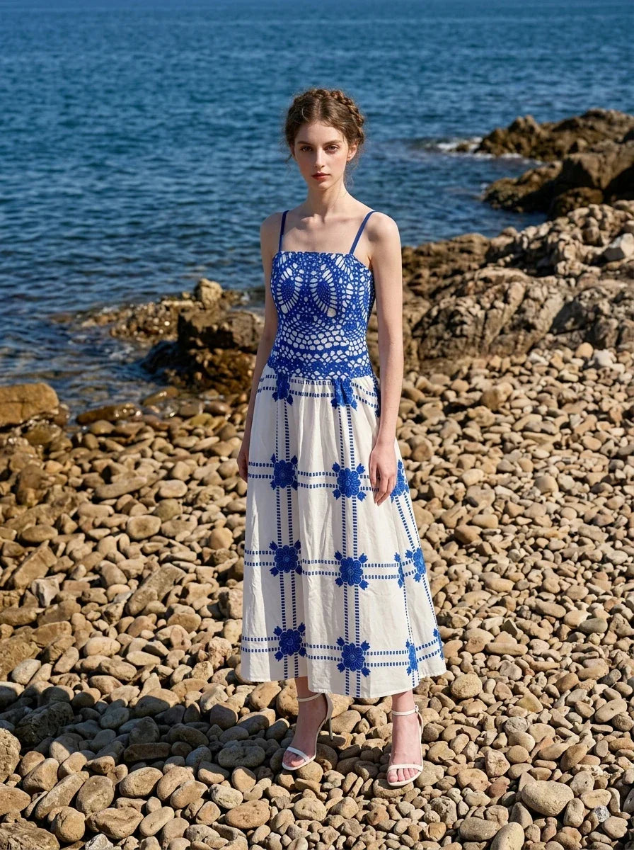Woman wearing a pink midi dress with a tropical print and spaghetti straps on a rocky beach