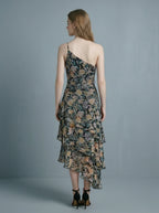 Back view of a woman in a floral print one-shoulder chiffon dress with a tiered, asymmetrical ruffle skirt.