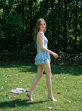 Woman walking in a light blue ruffled halter dress in a grassy field