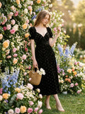 Woman standing next to a floral wall wearing a black floral burnout velvet midi dress with puff sleeves.