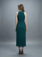 Back view of a woman in a dark green sleeveless halter neck sheath dress with ruched detailing and a high slit