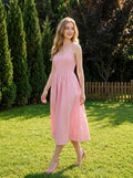 Woman wearing a pink midi dress with spaghetti straps and a square neckline, walking on grass in a garden.