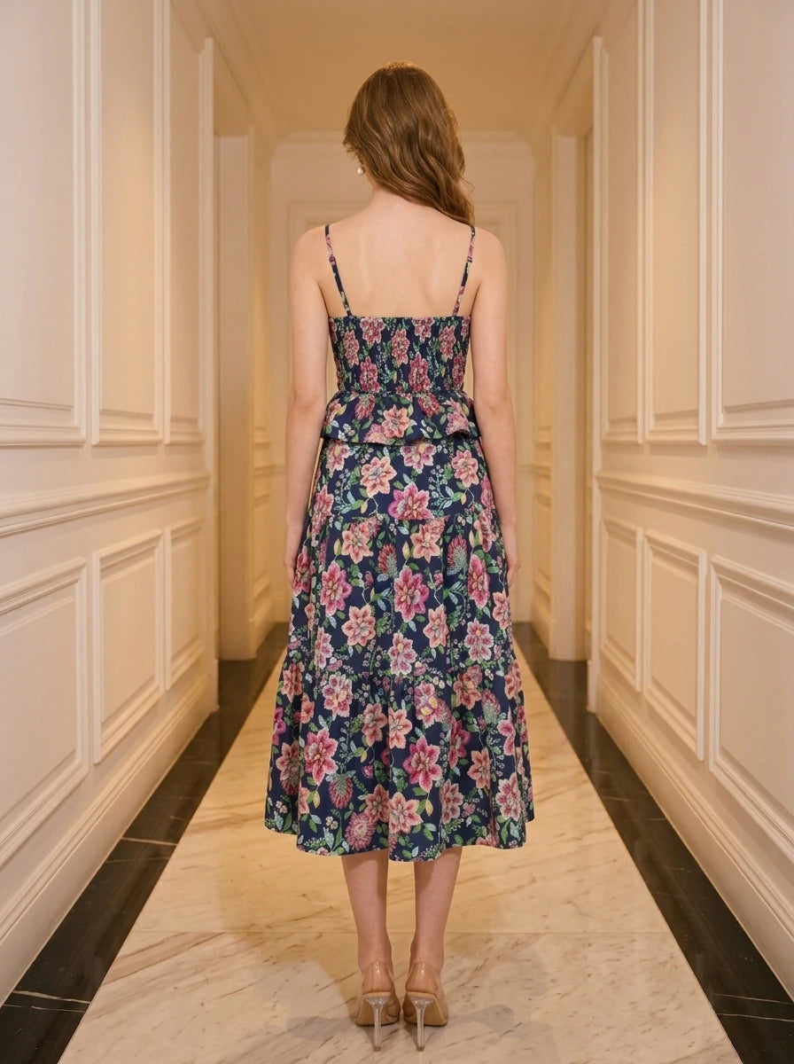 Woman wearing a navy floral print midi dress with spaghetti straps and a peplum waist, standing in a hallway.