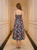 Back view of a woman in a navy floral print midi dress with spaghetti straps and a peplum waist, standing in a hallway.