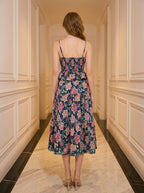 Back view of a woman in a navy floral print midi dress with spaghetti straps and a peplum waist, standing in a hallway.