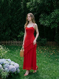 Woman in a red, floor-length, spaghetti strap dress with ruffle detailing, standing in a garden setting with hydrangeas and a wicker basket