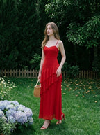 Woman in a red, floor-length, spaghetti strap dress with ruffle detailing, standing in a garden setting with hydrangeas and a wicker basket
