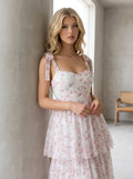 Close-up of a woman wearing a white and pink floral print tiered midi dress with tie shoulder straps