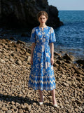 Woman wearing a blue floral print midi dress with puff sleeves, standing on a rocky beach with the ocean in the background.