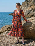 Woman standing on a rocky beach wearing a navy blue long-sleeved floral print midi dress, with the ocean in the background.