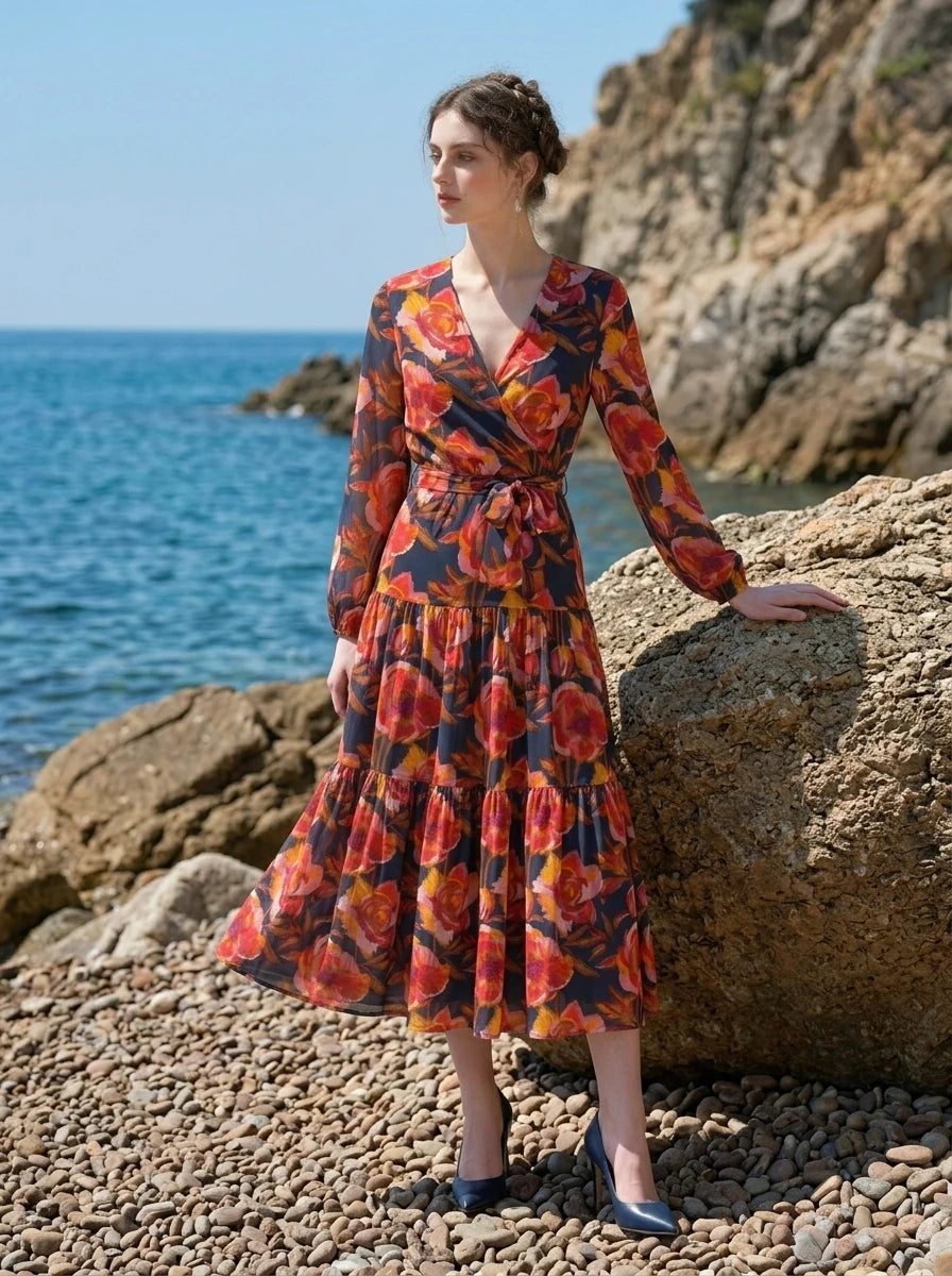 Woman standing on a rocky beach wearing a navy blue long-sleeved floral print midi dress, with the ocean in the background.