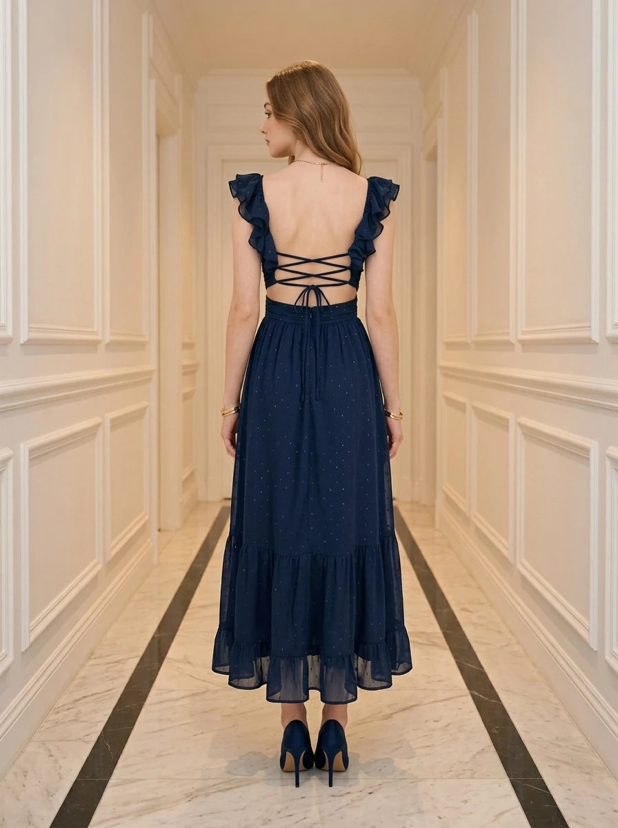 Woman wearing a navy blue polka dot midi dress with a deep V-neck and ruffled straps, standing in a hallway.