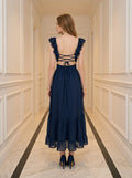 Rear view of a woman in a navy blue polka dot midi dress with an open back and criss-cross straps, standing in a hallway.