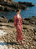 Woman standing on a rocky shore wearing a long, floral print, V-neck dress with long balloon sleeves.