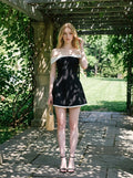 Woman in a black off-the-shoulder dress with white trim walking in a garden