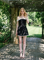 Woman in a black off-the-shoulder dress with white trim walking in a garden