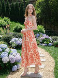 Woman posing in a cream and coral floral print halter neck midi dress in a garden setting
