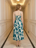 Back view of a woman in a cream and teal floral print midi dress with a smocked back and adjustable spaghetti straps.