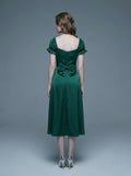 Rear view of a woman in a green satin midi dress with a large bow detail at the back and puff sleeves.