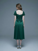 Rear view of a woman in a green satin midi dress with a large bow detail at the back and puff sleeves.