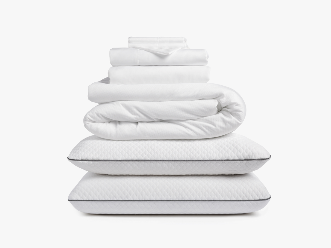 Stacked white bedding including sheets, duvet, and pillows