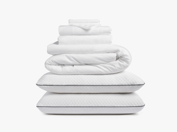 Stacked white bedding including sheets, duvet, and pillows