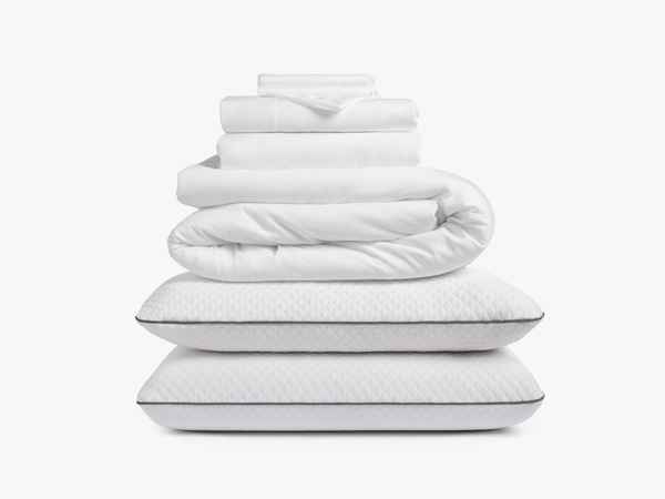 Stacked white bedding including sheets, duvet, and pillows