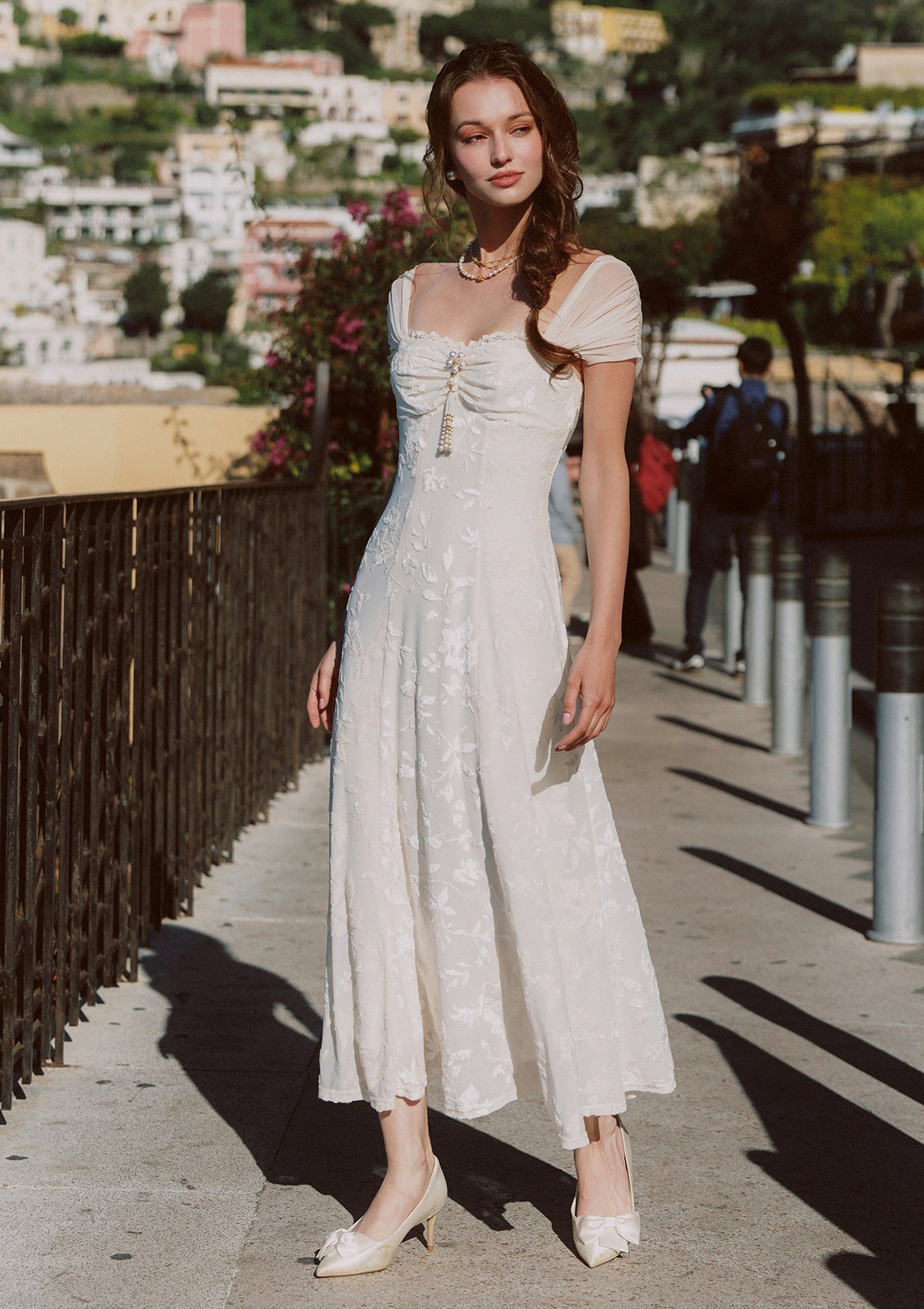 Woman wearing a cream-colored jacquard midi dress with off-the-shoulder neckline and sheer cap sleeves, standing outdoors.