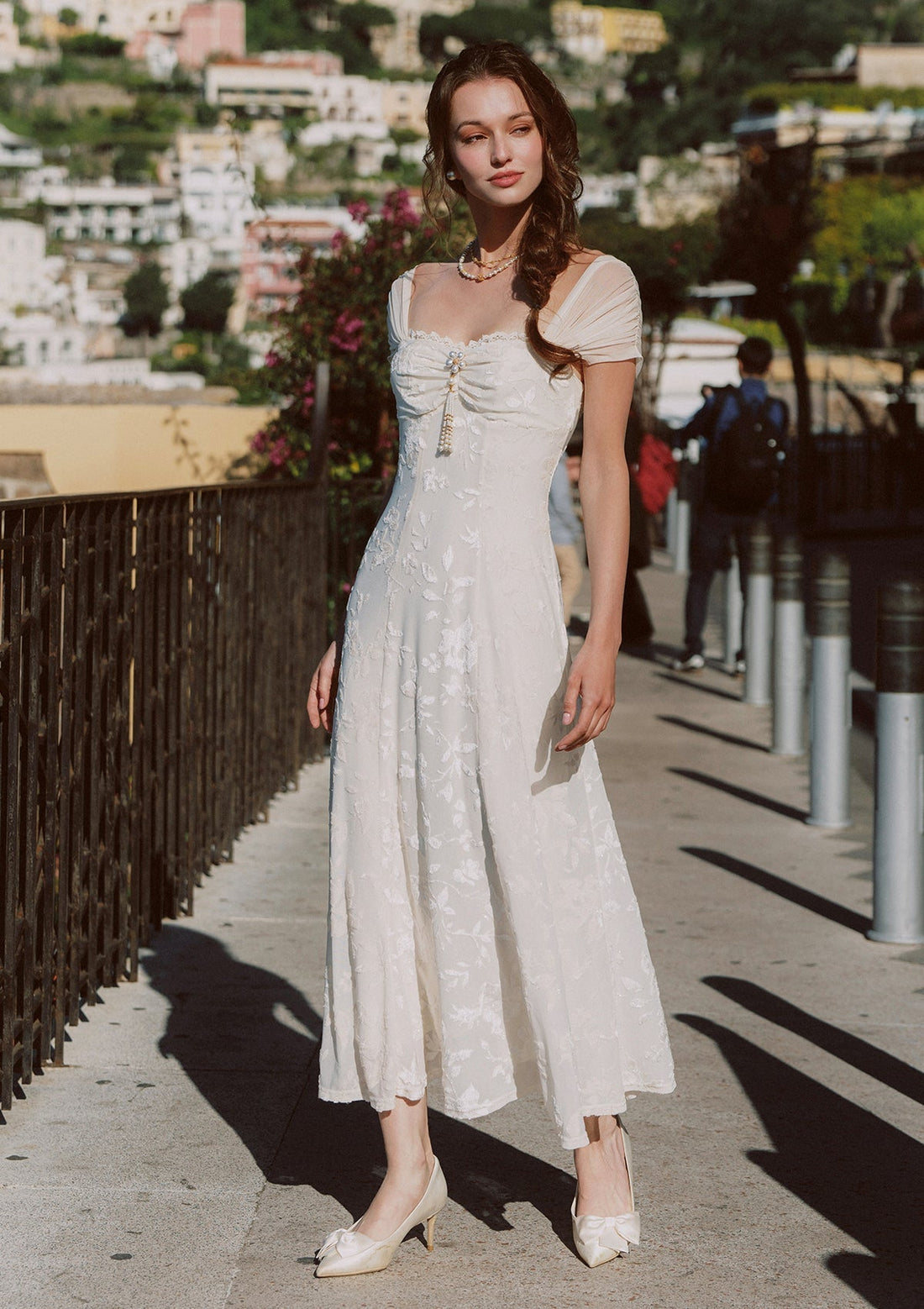 Woman wearing a cream-colored jacquard midi dress with off-the-shoulder neckline and sheer cap sleeves, standing outdoors.