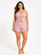 Plus-size woman wearing a pink ribbed knit cami top and shorts pajama set with lace trim and bow accents