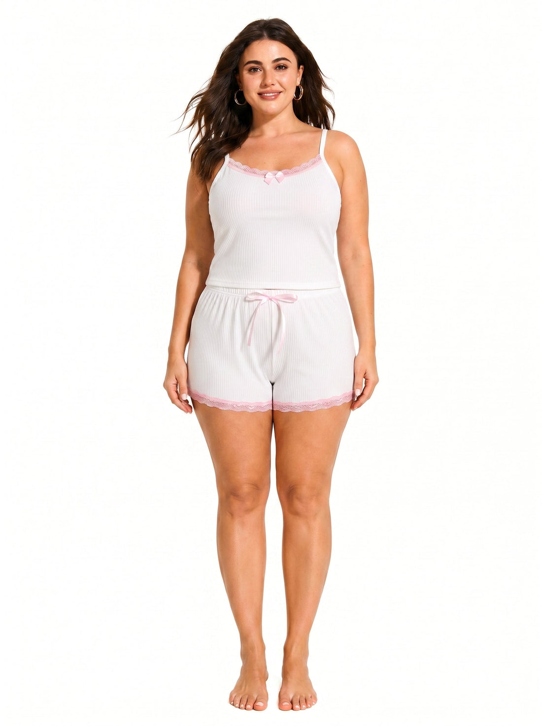 Woman wearing a white ribbed camisole and shorts pajama set with pink lace trim and bow details, front view.
