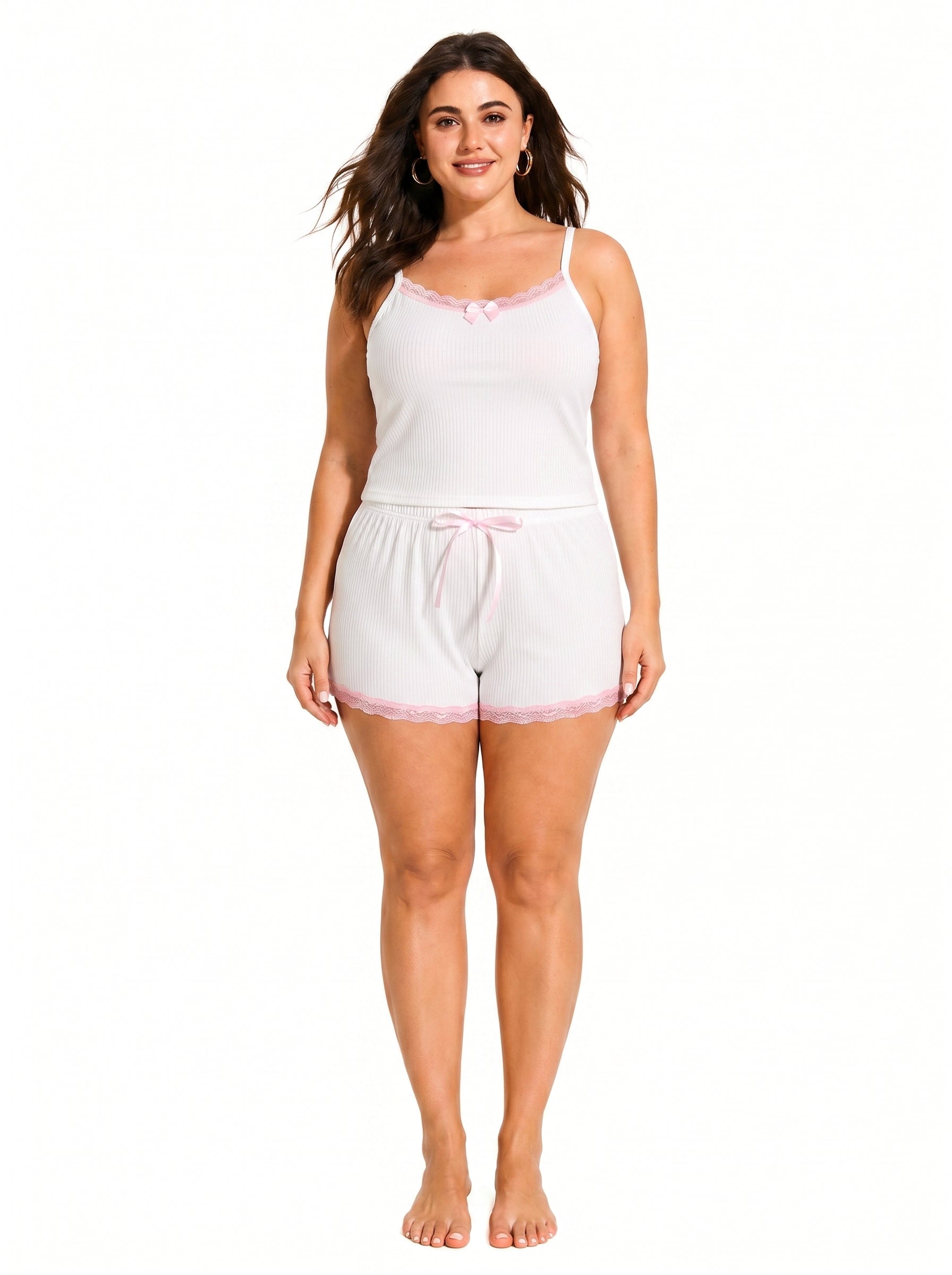 Woman wearing a white ribbed camisole and shorts pajama set with pink lace trim and bow details, front view.