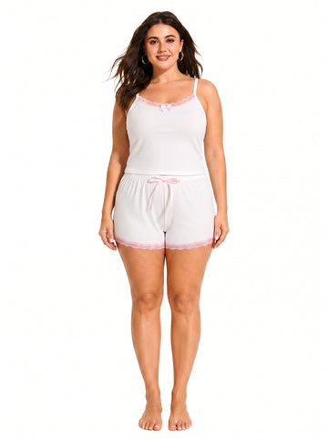 Woman wearing a white ribbed camisole and shorts pajama set with pink lace trim and bow details, front view.
