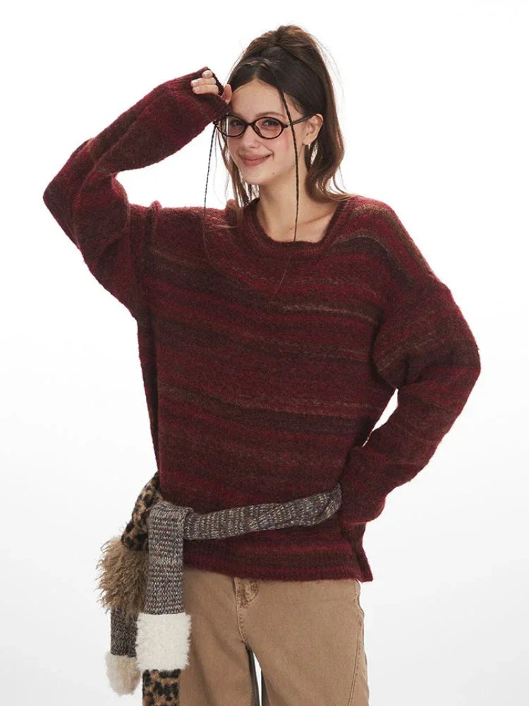 Woman with glasses adjusting her hair while wearing a maroon and brown striped oversized knit sweater.